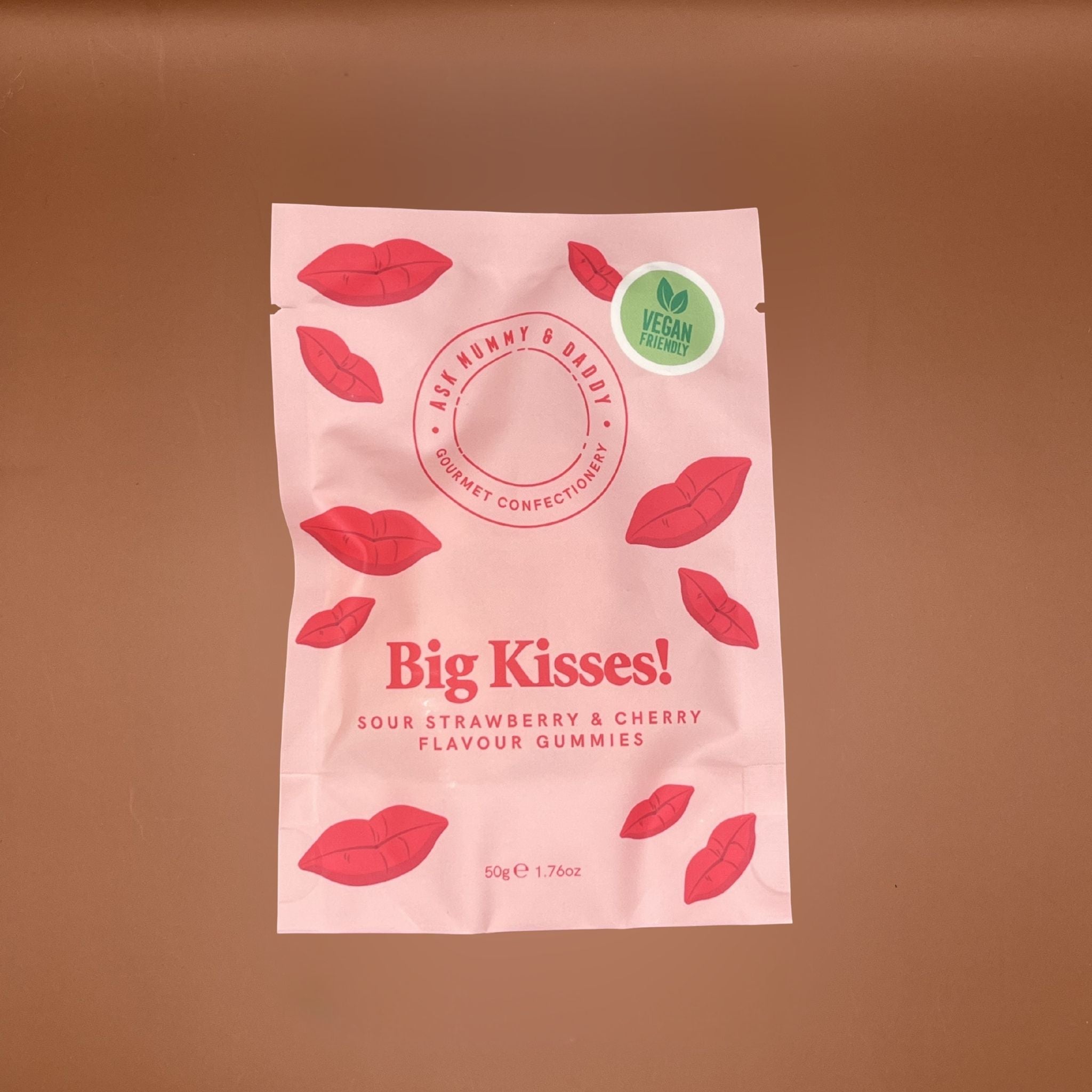 Pink packaging of 'Big Kisses!' gummies with red lip designs on a brown background