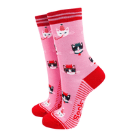 Pair of pink socks with red toes, heels, and cuffs, decorated with cat faces wearing party hats.