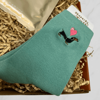 Close-up of green dachshund socks with heart design inside letterbox gift box.